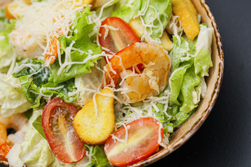 Caesar salad with shrimp in a bowl on a black background.