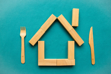Eco-friendly house made of wooden blocks with wooden knife and fork on a blue background. Planet care concept. Flat lay, top view, copy space.