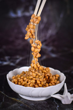 'Natto', a traditional Japanese food made from fermented soybeans drawing sticky strings on chopsticks on dark background