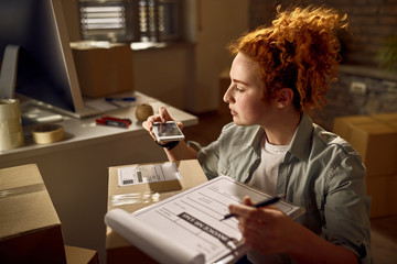 Yung woman preparing packages for delivery and scanning bar code with smart phone.