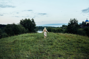 A girl runs along a lush green field to a pond