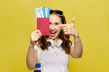 The girl holds a passport with tickets and points a finger at them.