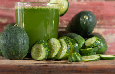 Juice and fresh fruits and sliced green cucumber (Cucumis sativus) on aged red wooden background