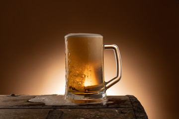 Fresh beer in a mug on a wooden table with spilled foam, a nice dark orange wall as a background in a restaurant