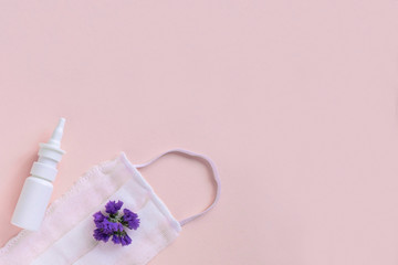 Seasonal spring summer allergy flowers concept. White spray container with purple flowers and medical protective mask on pink background. Creative flat lay composition, copy space