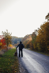 Fototapeta premium Lonely guitarist looking at empty country road in autumn.