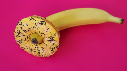 Sweet donut and banana on pink color background. Sex and Erotic concept
