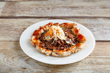White plate with soba buckwheat noodles and vegetables with chicken on a wooden table.