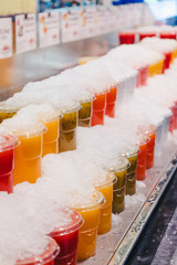 Fruit juice mix with ice arranged in plastic cups on a market stall with small fork inside, takeaway snack