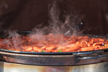 Sausages in their own juice on a large round pan from which steam comes