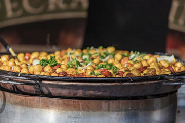 Potatoes with vegetables in a large round pan from which steam comes