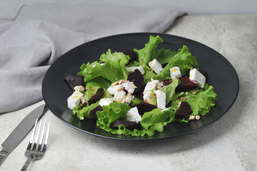 Salad with beets, soft cheese, nuts and green salad.  The concept of light and healthy dishes.  Light background.  Close-up.