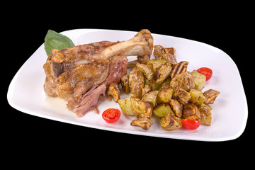 Tasty Pork Shanks with oven potatoes and cherry tomatoes, on a plate, isolated on black background