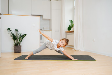 Six year old girl doing yoga at home, bending forward with legs wide apart