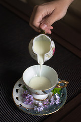 at home in the family tea room an old gilded mother of pearl porcelain service a hand in a glass with a plate pours fresh cow's milk from the milkman on the background of a wooden table