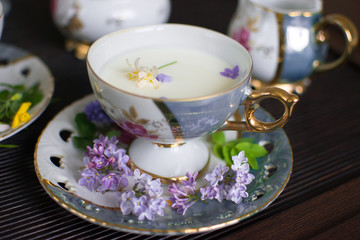 at home in the tea room an old gilded mother of pearl porcelain service in a glass with a plate filled with fresh cow's milk and decorated with bright wild flowers Apple lilac forget me nots yellow 