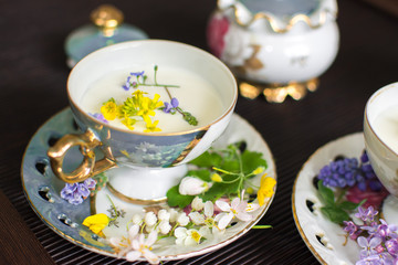 at home in the tea room an old gilded mother of pearl porcelain service in a glass with a plate filled with fresh cow's milk and decorated with bright wild flowers Apple lilac forget me nots yellow 