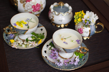 at home in the tea room an old gilded mother of pearl porcelain service in a glass with a plate filled with fresh cow's milk and decorated with bright wild flowers Apple lilac forget me nots yellow 