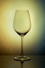 The crystal glass stands on the reflecting surface on a yellow graybackground. studio photo. product. Beautiful shadow from wine glass. macro photo