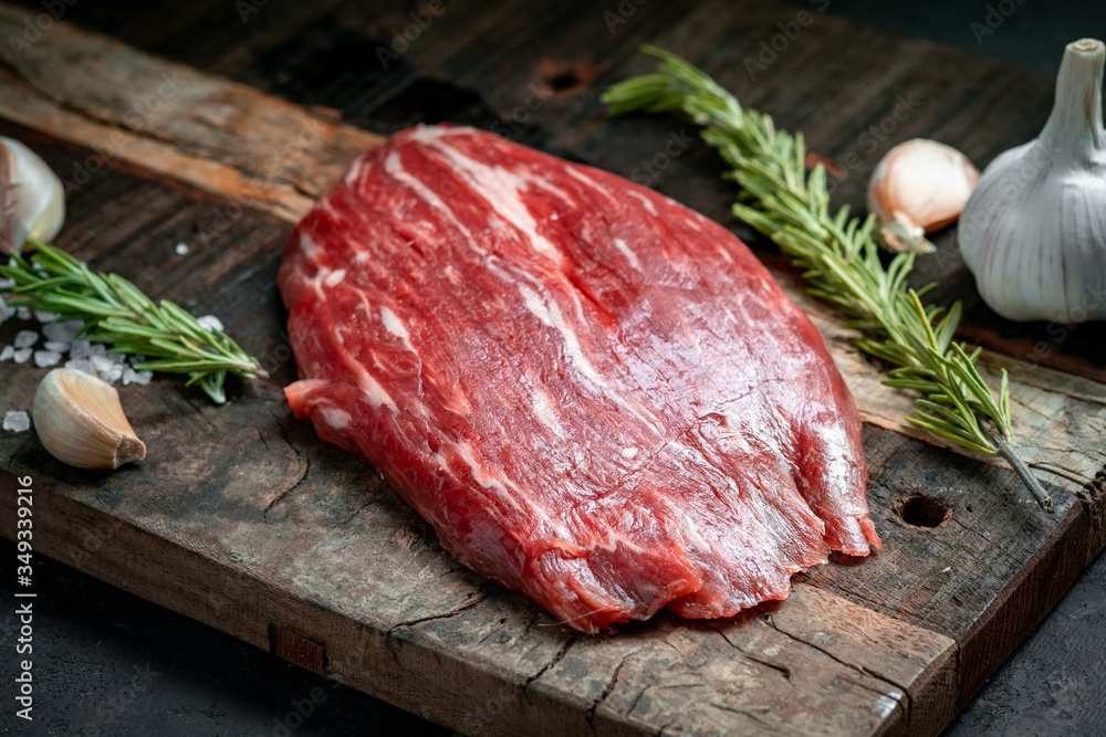 Wall mural raw flank beef steak and ingredients for cooking on a wooden board, close up