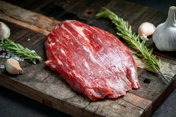 Poster Raw flank beef steak and ingredients for cooking on a wooden Board, close up © Andrey