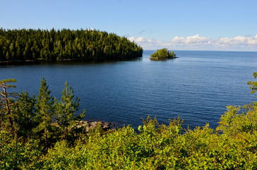 Blue, calm lake in Karelia, blue sky with white clouds. Islands with a green forest in the lake....
