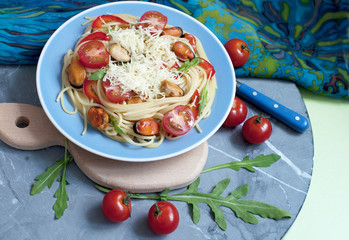 Spaghetti with mussels, parmesan cheese, tomatoes, arugula on gray background. Pasta with seafood