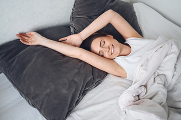 Attractive smiling young woman stretching in bed waking up alone happy concept, awake after healthy...