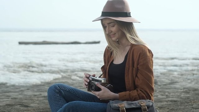Stylish girl sitting on the sand near the frozen sea. A woman uses an old retro camera and takes beautiful pictures of the landscape. happy girl travels and takes pictures on camera