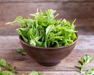 Fresh, ripe arugula in a clay bowl on a wooden table.