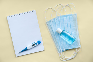 on a yellow background is an empty Notepad with an electronic thermometer and a number of medical protective masks, antiseptic for hands