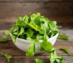 Fresh, ripe arugula in a ceramic white mask on a wooden kitchen table.