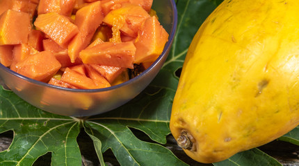 Papaya (Carica papaya L.) chopped in bowl and fresh fruit among papaya leaves