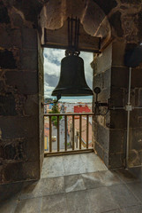 Fototapeta premium Top view through the slatted window from the high tower of the church. Outside the window are tiled roofs of historic buildings. Silhouette of a church bell in a window. La Laguna, Tenerife