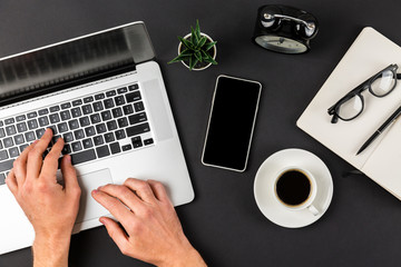 Overhead view of male businessman hands using laptop on abstract dark black office desk with coffee and eye glasses