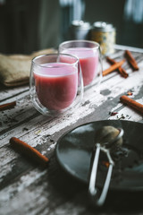Cup of pink tea in a clean white table with flowers and ingredients. Vertical view