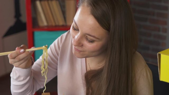 Girl Freelancer Eating Chinese Noodles Out Of Box In Home Office. Young Woman Eat Pan Asian Lunch With Chopsticks During Break In Workplace. Fastfood And Food Delivery. Diet Nutrition Office Worker.