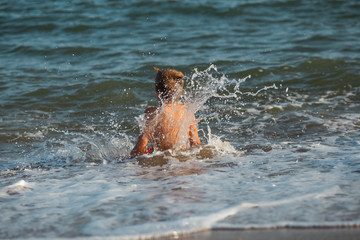 Fototapeta premium verano en la playa niño que salta y cae al agua del mar olas