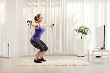 Fototapeta na wymiar Young female exercising with a resistance band while watching tv