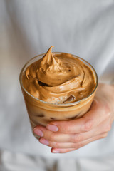 Dalgona coffee. Cold drink with ice. Whisk instant coffee, sugar and add in milk. Glass of coffee in girl hand. Woman barista making delicious summer beverage. Professional service