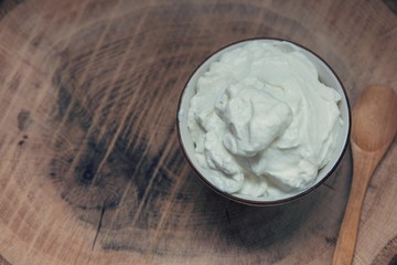 A bowl of yogurth with a wooden spoon on a wooden table, above vanyage point photography, close up