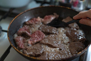 Pieces of meat are fried in a pan