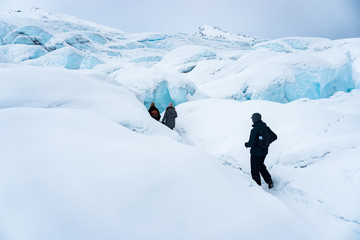 Fototapeta na wymiar Group of three hikers trekking on the snow in Matanuska Glacier, Alaska. They are following a path into the ice caves. Extreme adventure during winter holidays. Having fun in the mountains. 