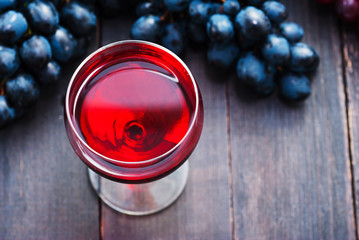 glass of red wine and grapes on black wooden table background