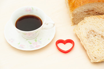 Homemade Brazilian bread sliced next to a red heart shape object and a cup of coffee. Isolated on light wooden background. Copy space. Concept: Celebration of Mother's Day and Valentine's Day.