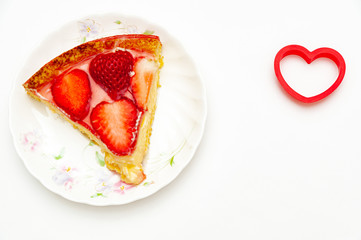 Delicious slice homemade strawberry tart with heart-shaped object on the side. Isolated on white background. Top view. Close-up. Copy space. Horizontal shot.