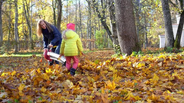 Woman and her little daughter girl playing with colorful autumn leaves in yard