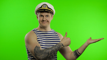 Young sailor man pointing to something with hands. Seaman guy in sailor's vest
