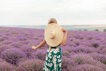 Woman in green dress and straw hat in her hands dancing at the field of lavender flowers on sunset. 
