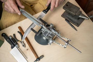 Making of a knife. Master sharpens a blade on the machine closeup in the Studio